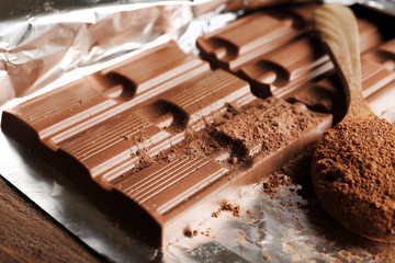 Bar of chocolate with cocoa on foil, closeup
