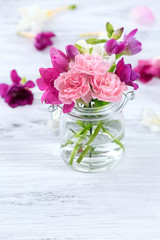Beautiful spring flowers in glass bottle on wooden background