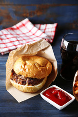 Tasty burger and french fries on plate, on wooden table background. Unhealthy food concept
