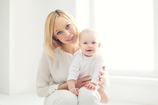 Portrait of happy young mom with baby at home in white room