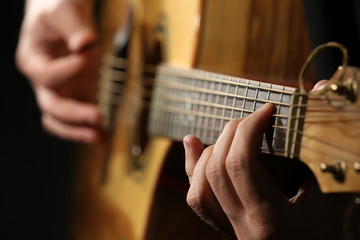 Young man playing on acoustic guitar on dark background