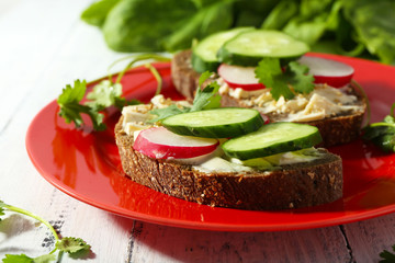 Delicious sandwiches with vegetables and greens on plate on table close up