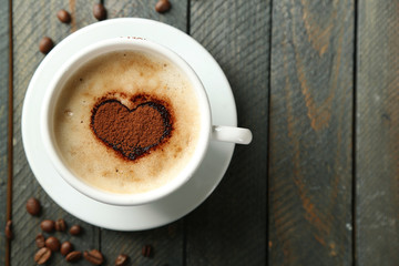 Cup of cappuccino with heart of cocoa on wooden table