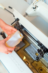 Female hand adding oil in sewing machine. Maintenance.