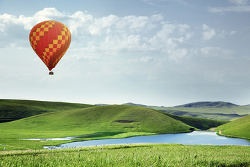 Air balloon flying over the meadows with lake