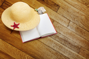 Straw hat with book and red starfish on shabby wooden background