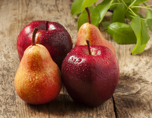 Red apples and yellow pears with drops of water on wooden table,