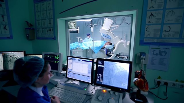 Assistant controls a cardio surgery in front of monitors