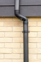 Close up of a black drainage pipe and clip on a brick wall