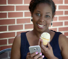 Beautiful African American woman with cell phone and cupcake
