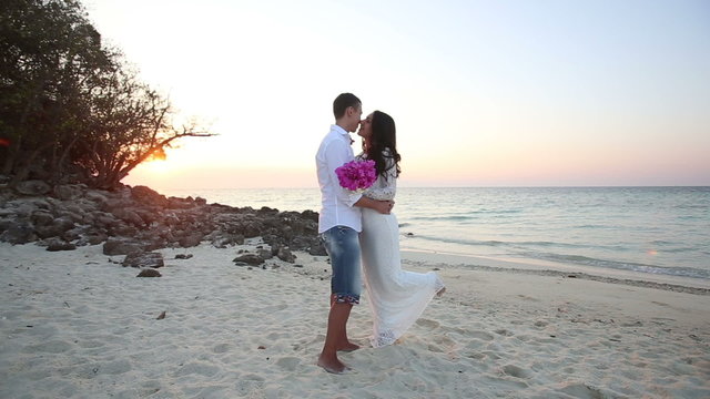 brunette bride and handsome groom barefoot hug at sand beach