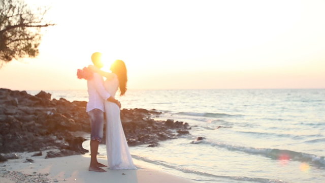 bride and groom hug against backlight at beach at dawn	