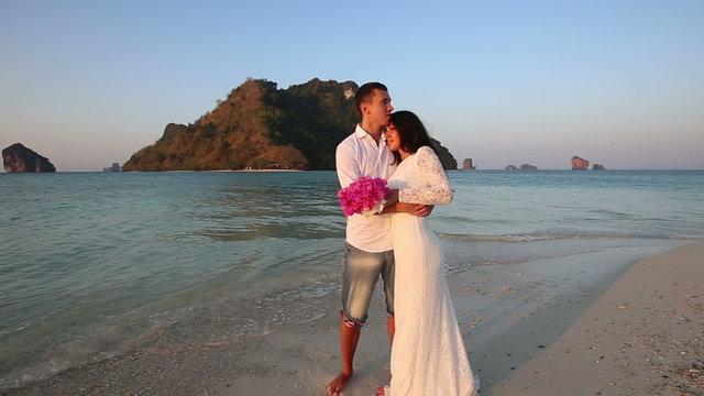 bride and groom hug standing in water against island	