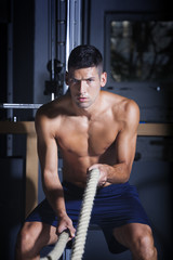 Muscular man in gym with battle ropes