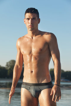 Muscular man in swim briefs getting out of water