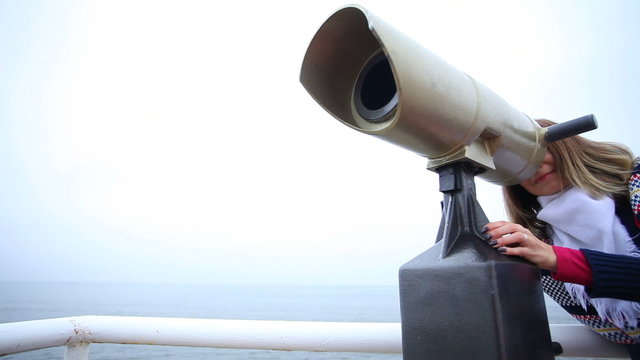 Woman looking through the tourist binoculars at the sea shore