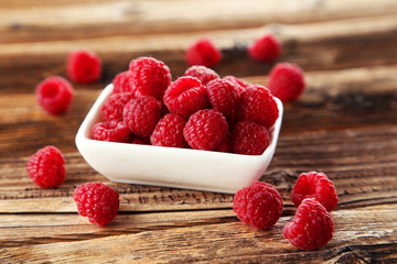 Raspberries in bowl on brown wooden background