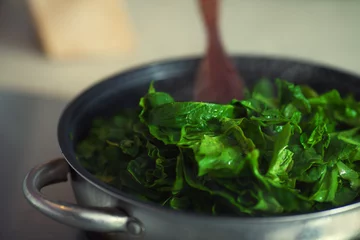 Schapenvacht deken met foto Koken Vegetarisch voedselconcept. Verse spinazie koken in metalen pot.