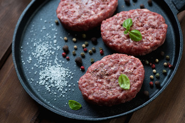 Raw beef cutlets with pepper and salt in a frying pan, close-up