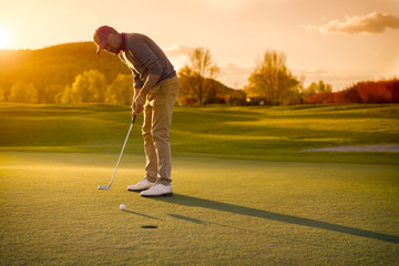 Männlicher Golfspieler, der bei Sonnenuntergang setzt.