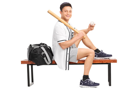 Baseball player holding a bat seated on bench