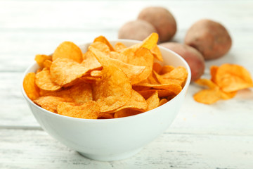Potato chips in bowl on white wooden background