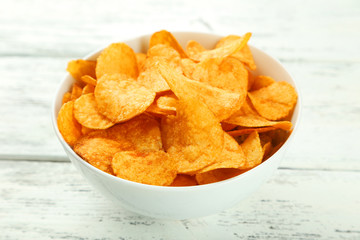 Potato chips in bowl on white wooden background
