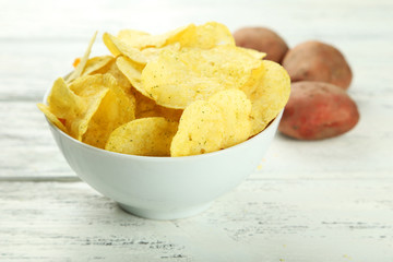 Potato chips in bowl on white wooden background
