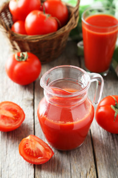 Fresh red tomatos in basket and juice on grey wooden background