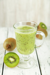 Fresh kiwi smoothie in glass on white wooden baclground