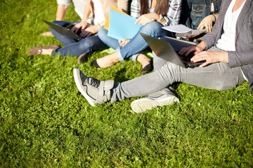 close up of students with laptop sitting on grass
