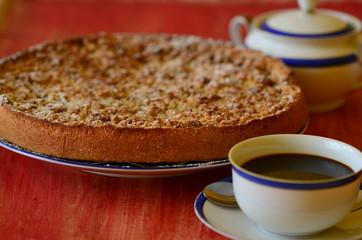 Plum crumble tart with cup of coffee and sugar bowl.