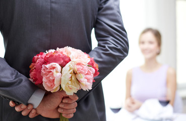 close up of man hiding flowers behind from woman