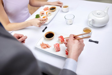 Fototapeta na wymiar close up of couple eating sushi at restaurant
