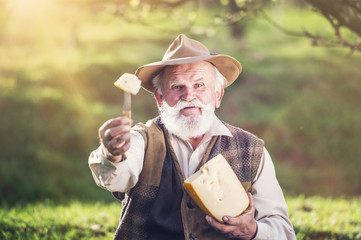 Farmer cutting and eating cheese outside in green nature