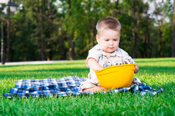child in the construction helmet sits on a grass playing