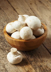 White mushrooms in a bowl on wooden table, selective focus
