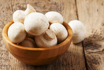 White mushrooms in a bowl on wooden table, selective focus