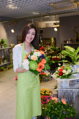 Fototapeta premium cheerful young woman florist selling flowers in flower shop