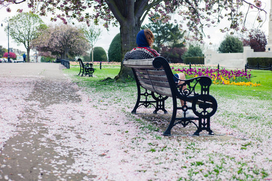 Woman sitting on bench in park with cherry blossom