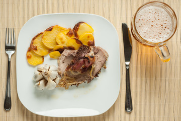 roasted pork with garlic and potatoes on white plate