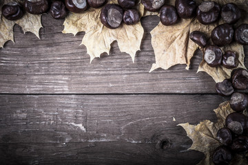 Chestnuts and autumn leaves on a old wooden table. Space for tex