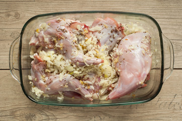 raw rabbit meat in roaster with onion cumin and garlic on wooden