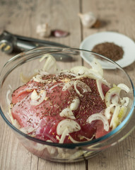 pork meat in roaster with onion cumin and garlic on wooden table