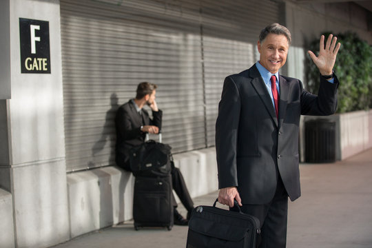 Business man waves hello with a smile at the airport from business trip