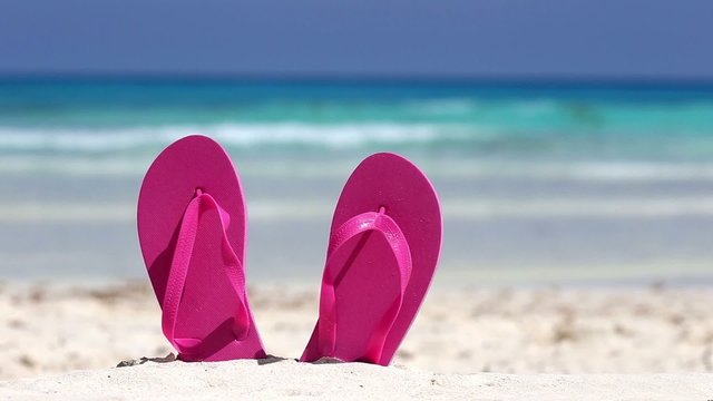 Pink flip flops on white sandy beach near sea waves
