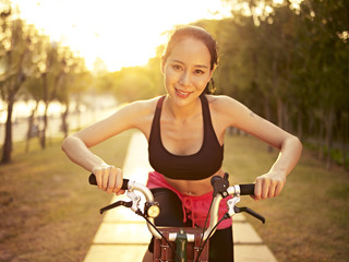 young asian woman riding bike outdoors at sunset