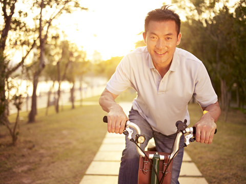 asian man enjoying bicycle ride outdoors at sunset
