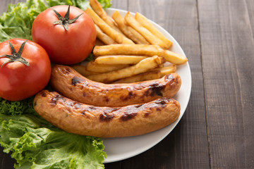 grilled sausage and vegetables with french fries on wooden backg