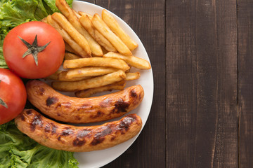 grilled sausage and vegetables with french fries on wooden backg